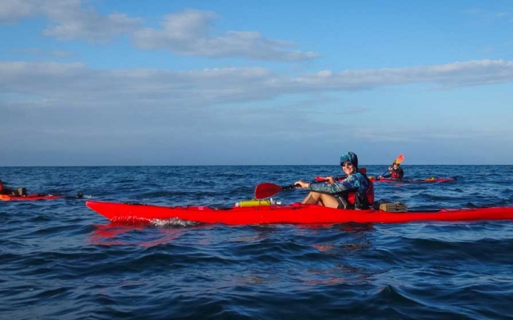 three red kayaks are paddled by outward bound students on a vast blue ocean with a blue sky above.
